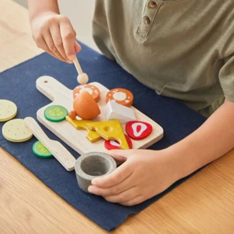 PlanToys Cheese & Charcuterie Board, wooden play set with brie, gouda, salami, crackers, and cutting board on a white background