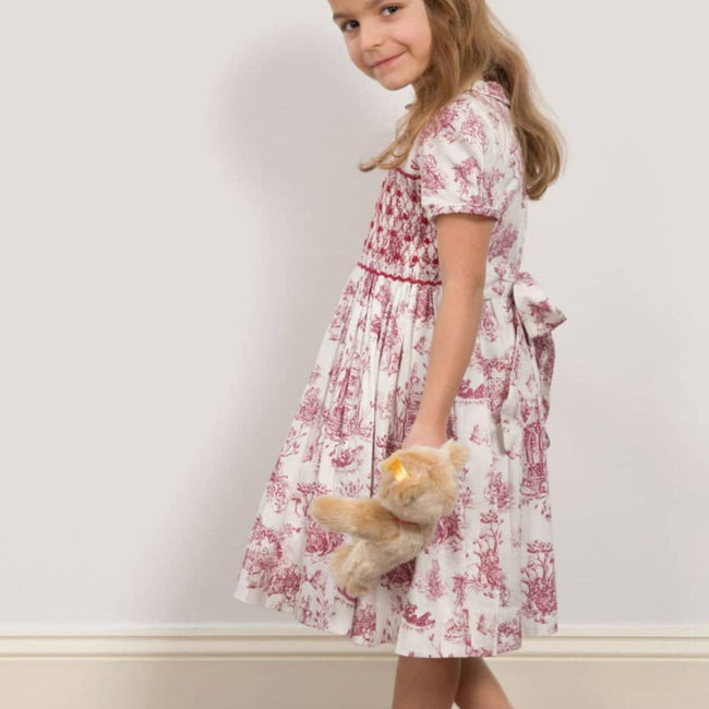 Philomena Smocked Toile de Jouy Dress - Burgundy / White, worn by toddler girl showing toile print and sash tie at waist